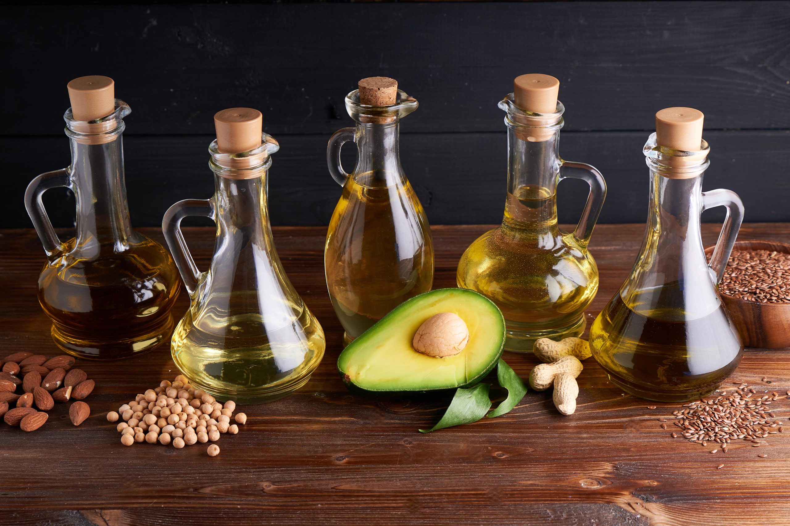 useful vegetable oils in glass bottles. avocado oil, chickpea oil, linseed oil, peanut oil, almond oil. dark wooden background